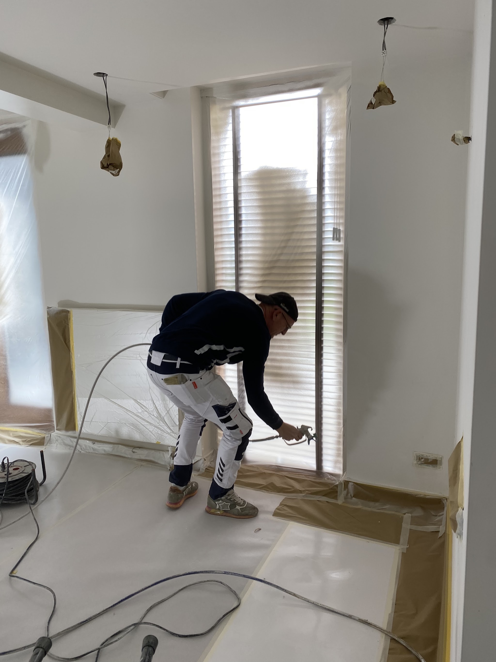 Een schilder met mondkapje spuit een muur in een afgeplakte kamer